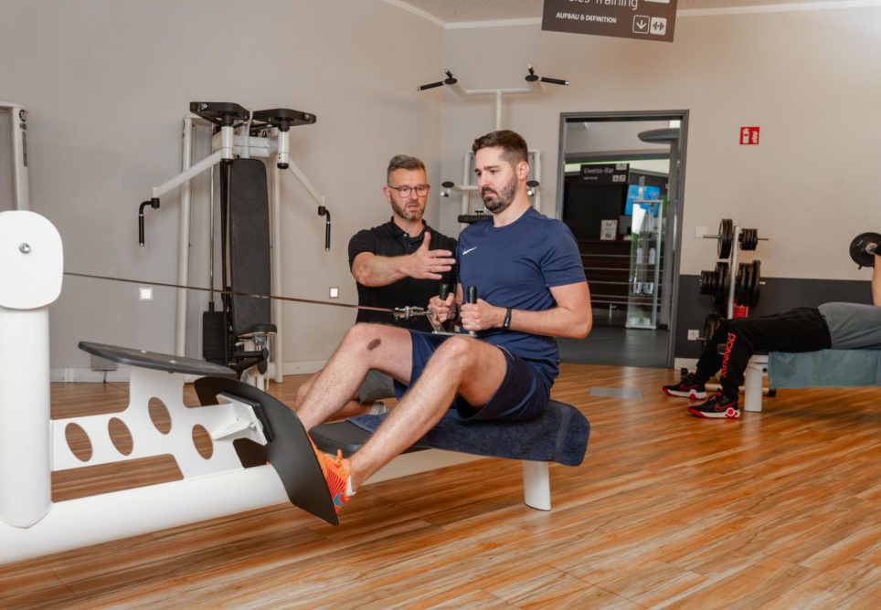 Im LIFE Fitness Oldenburg: Ein Coach unterstützt ein Mitglied beim Rückentraining an der Ruderstation für optimale Ergebnisse und gesunde Haltung.